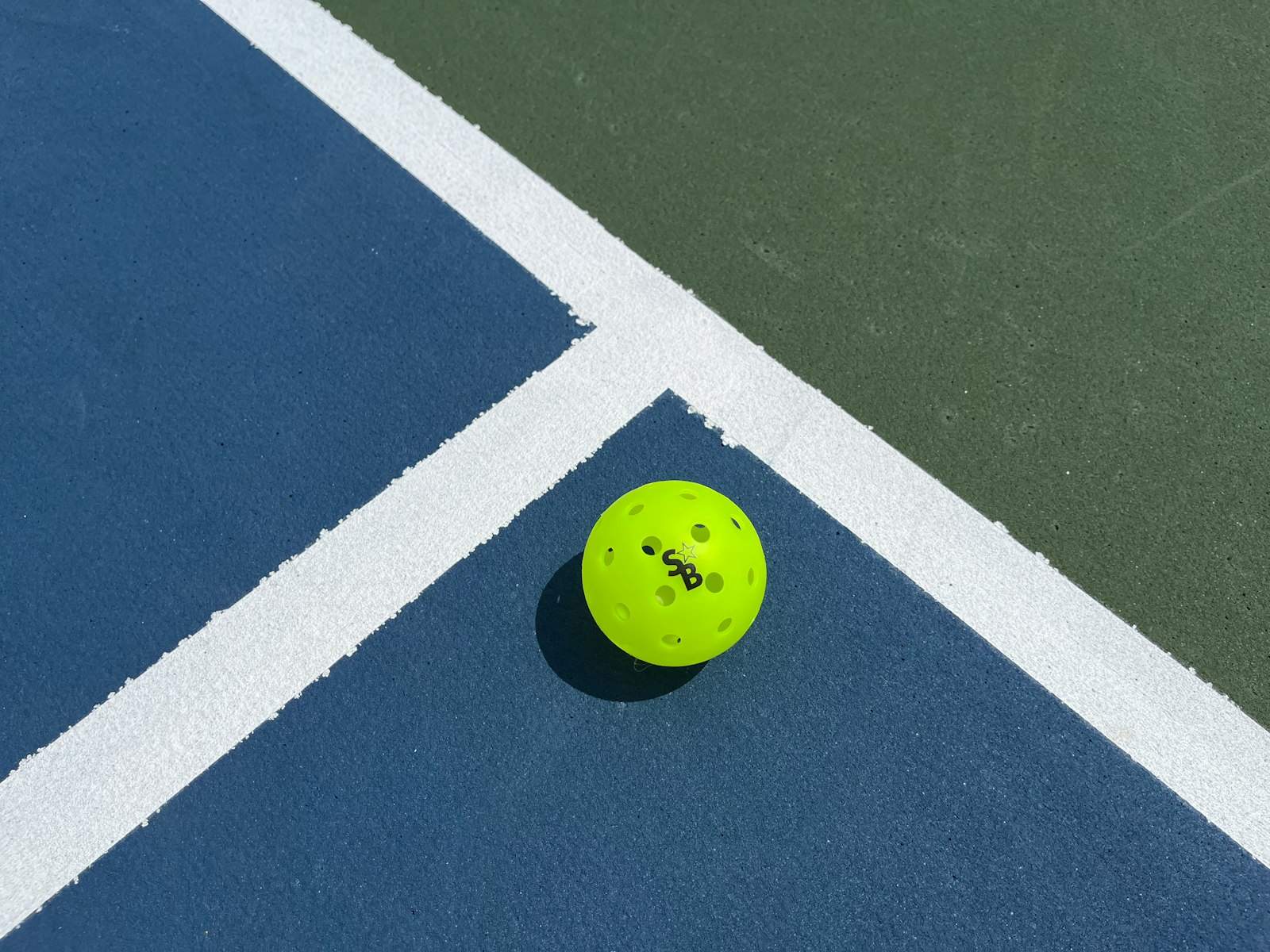 Close-up of a yellow pickleball on a blue and green court with crisp white striping